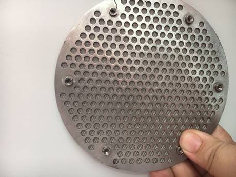 Une main tient une forme ronde a perforé le disque de filtre aggloméré par métal.